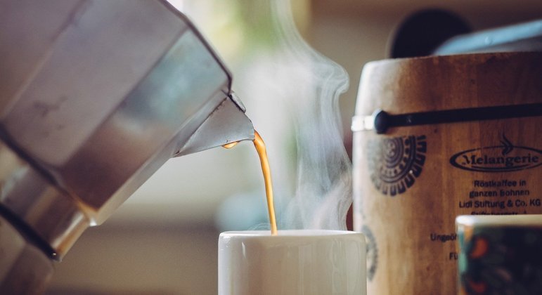 Só o café pode me refrescar. mulher afro-americana sonolenta e cansada  cobre metade do rosto com a palma da mão, tem expressão triste, fecha os  olhos, carrega um copo descartável de bebida com cafeína, continua  trabalhando.