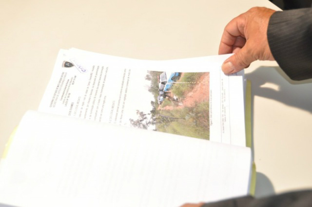 Delegado mostra inquérito com as imagens do local onde o corpo da vítima foi encontrado. (Foto: Marcelo Calazans)