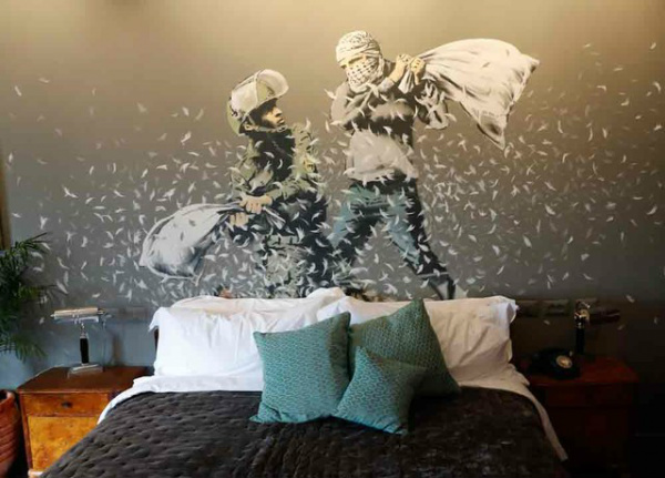 Banksy abre hotel com 'pior vista do mundo' em frente ao muro israelense na Cisjordânia Grafite em quarto do hotel Walled Off, do artista Banksy, mostra guerra de travesseiros entre soldado israelense e manifestante palestino (Foto: Thomas Coex/AFP)