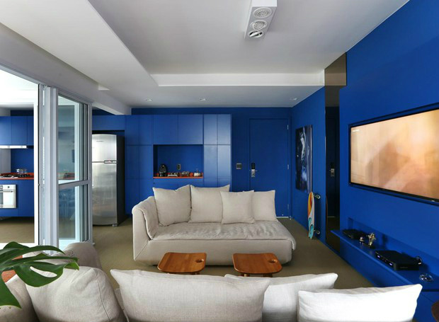 Apartamento pequeno, funcional e azul Os armários da cozinha seguem em linha contínua até a área social “alongando” o ambiente. Repare na bancada instalada na marcenaria. Execução Formas Móveis. Ela é usada como apoio para o café e bar (Foto: Mariana Orsi/Divulgação)