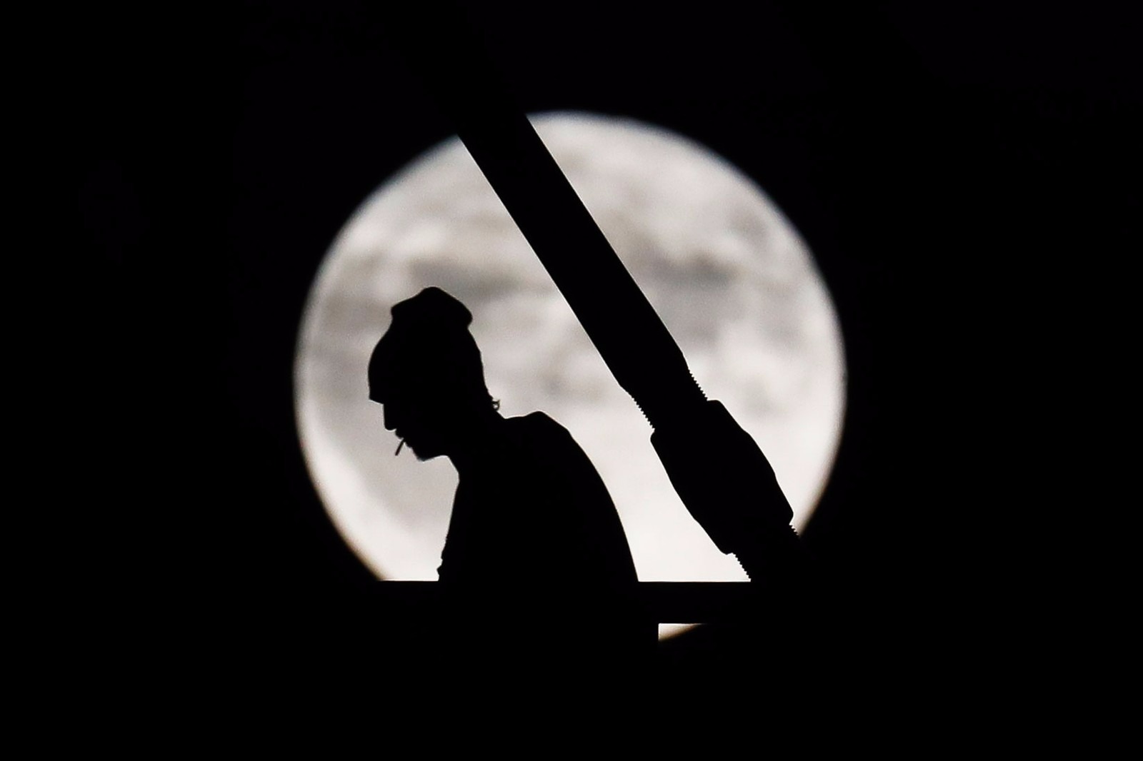 Como surgiu a superstição da sexta-feira 13? Pedrestre caminha em Cincinnati, Ohio, nos EUA, com a lua cheia ao fundo (Foto: John Minchillo/AP)